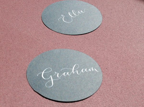 Multiple black circular table settings with names written in white ink in calligraphy for wedding or event
