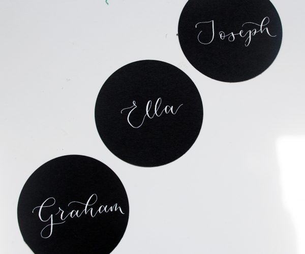 Multiple black circular table settings with names written in white ink in calligraphy