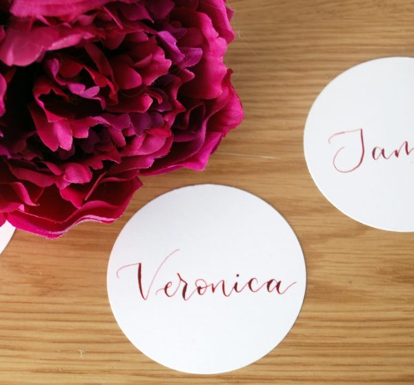 White circular disc event table setting with name handwritten in pink ink in calligraphy