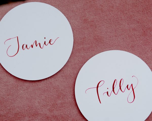 White circular disc event table setting with name handwritten in pink ink in calligraphy with pink background