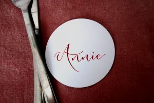 Wedding table setting, white circular name tag with pink writing next to knife and fork