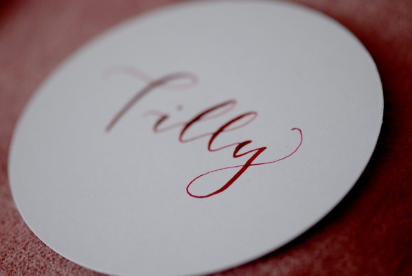 White circular disc wedding place setting with name handwritten in pink ink in calligraphy