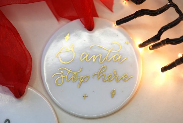 Metallic gold ink on personalised bauble that says Santa stop here with red ribbon