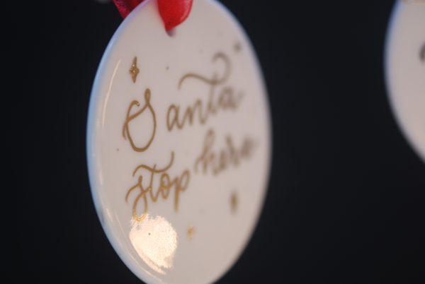 Metallic gold ink on personalised bauble that says Santa stop here with red ribbon