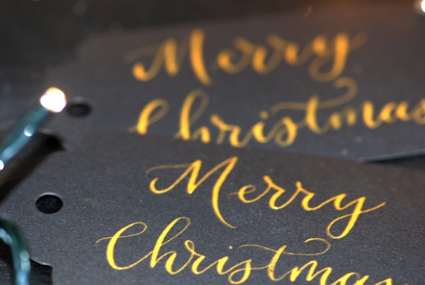 Black card gift tags with Merry Christmas written in gold ink and calligraphy